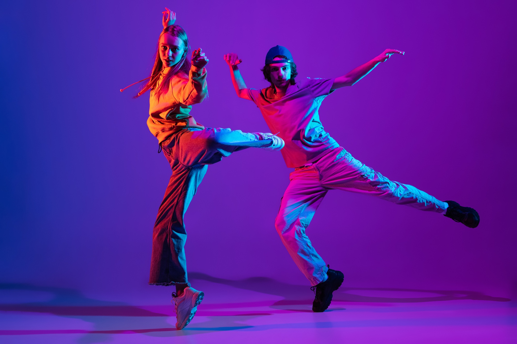 Two dancers, young man and woman dancing hip-hop in casual sports youth clothes on gradient purple